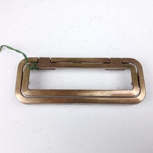 Puede incluir: Un tirador de cajón rectangular de latón de doble capa con un acabado liso y pulido.