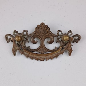 Puede incluir: Tirador de cajón de latón adornado con un diseño de volutas decorativas y dos pomos redondos. El tirador tiene un aspecto vintage y sería una gran adición a cualquier proyecto de decoración del hogar.