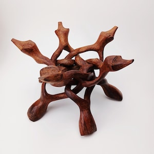 May include: A handcrafted, wooden decorative bowl stand. The stand is made of intricately carved, interlocking pieces of dark brown wood. The design features multiple curved arms that extend outward, creating a unique and artistic display piece. The stand is designed to hold a bowl or other decorative items.