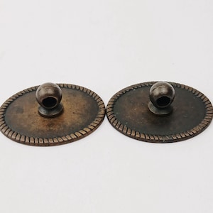 Puede incluir: Dos tiradores de cajón ovalados de bronce antiguo con un borde decorativo en forma de cuerda y un pomo redondo. Los tiradores son de un color bronce cálido y envejecido, lo que sugiere una estética vintage. Los pomos están centrados en las placas ovaladas.