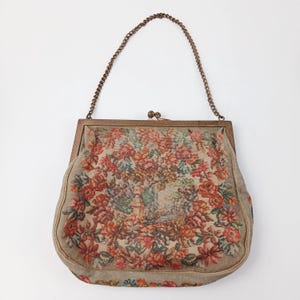 Puede incluir: Bolso de mano vintage de tapiz con un diseño floral en tonos rojos, naranjas y verdes. El bolso tiene un marco de metal y un asa de cadena. El tapiz representa una escena de jardín. Un accesorio clásico.