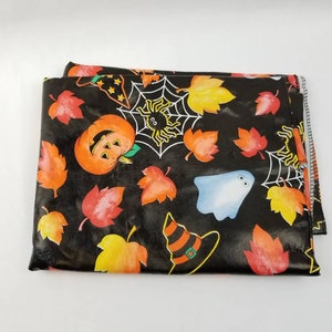Op de afbeelding: Zwarte stof met een Halloween-thema met pompoenen, geesten, spinnen en bladeren. De stof heeft een glanzende, bijna plastic-achtige afwerking.