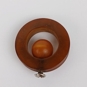 May include: A brown, circular object with a smaller, spherical object inside. The outer ring has a ridged texture, and a small, silver screw is attached at the bottom. The inner sphere is a lighter shade of brown.