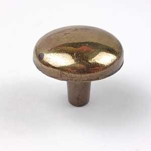 May include: A single, antique-style cabinet knob with a rounded, mushroom-shaped head. The knob has a tarnished, brassy finish with a short, cylindrical stem. The knob is set against a plain white background.