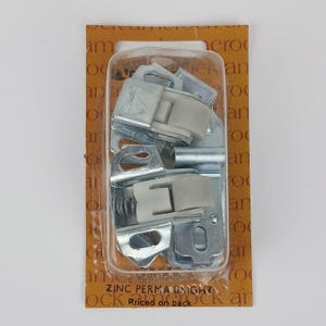 May include: A package of zinc-plated Perma Bright cabinet door rollers. The rollers are silver-colored with white plastic components. The packaging is a clear plastic blister pack on a brown cardboard backing.