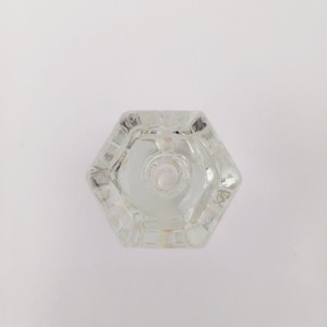 May include: A clear, hexagonal glass knob with a central hole. The knob has a multifaceted design, reflecting light. The object is likely a decorative element for furniture or a cabinet.