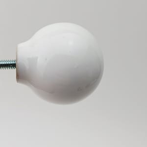 以下が含まれることがあります： 金属ネジが付いた、白くて丸いセラミック製のキャビネットノブ。ノブは滑らかで光沢のある仕上がりで、クラシックでシンプルなデザインです。ネジは銀色で、ねじ切りされており、取り付けの準備ができています。引き出しやキャビネットに適しています。直径約4cm。