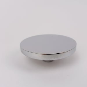 May include: A polished, silver-coloured, circular object with a flat top and a short, rounded base. The object has a reflective surface, possibly made of metal. The design is simple and modern, with clean lines and a minimalist aesthetic. The object is likely a lid or a stopper.