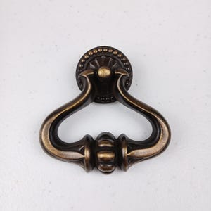 May include: A brass door pull with a decorative ring and a heart-shaped design.