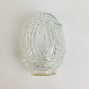 May include: Clear glass light fixture shade with a textured, oval design. The shade has a rounded top with a woven pattern and a flared base. The glass is transparent, allowing light to pass through.