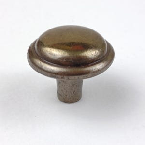 May include: A bronze-colored cabinet knob with a rounded top and a textured, cylindrical base. The knob has a layered design on the top and a slightly distressed finish, suitable for furniture hardware.