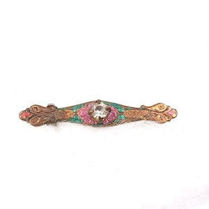 Puede incluir: Broche de barra vintage con una piedra central transparente y detalles de esmalte de colores. El broche presenta una base de metal color bronce con detalles de esmalte rosa, verde y rojo. El diseño es simétrico, con adornos decorativos en cada extremo.