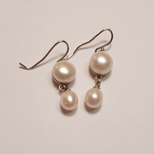 May include: A pair of silver dangle earrings with two white pearls on each earring.