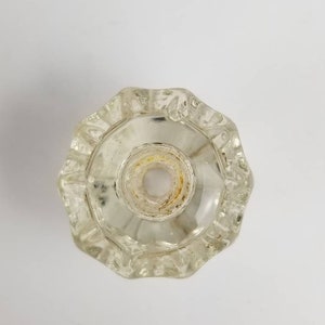 Op de afbeelding: Een heldere glazen deurknop met een facetgeslepen ontwerp. De knop heeft een gat in het midden voor een schroef.