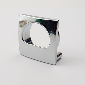 May include: A polished chrome cabinet pull with a square face and a circular aperture. The pull features a small, cylindrical post for mounting. This hardware is designed for use on drawers or cabinet doors, and is a modern design.