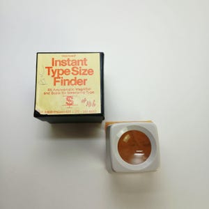 May include: An 8X achromic magnifier and type size finder with a square black box featuring the text "Improved! Instant Type Size Finder 8X Anchromatic Magnifier and Scale for Measuring Type. H. SHERR ENGRAVERS / 212 - 242-8650".