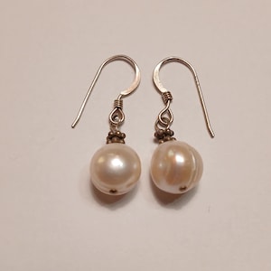 May include: A pair of silver earrings with white pearl drops. The pearls are round and have a slight iridescent sheen.