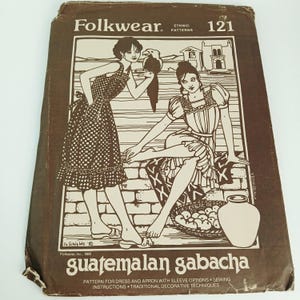 May include: A brown and white sewing pattern envelope for a Guatemalan gabacha, featuring illustrations of two figures in dresses and aprons, a bird, and a basket of fruit. The text reads Folkwear, 121, Ethnic Patterns, and Guatemalan gabacha.