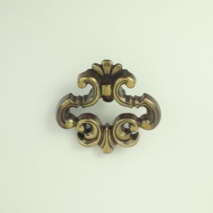 May include: An antique brass drawer pull with an ornate floral design. The pull has a curved handle with scrollwork and a central floral accent. This hardware is suitable for cabinets, drawers, or furniture restoration projects.