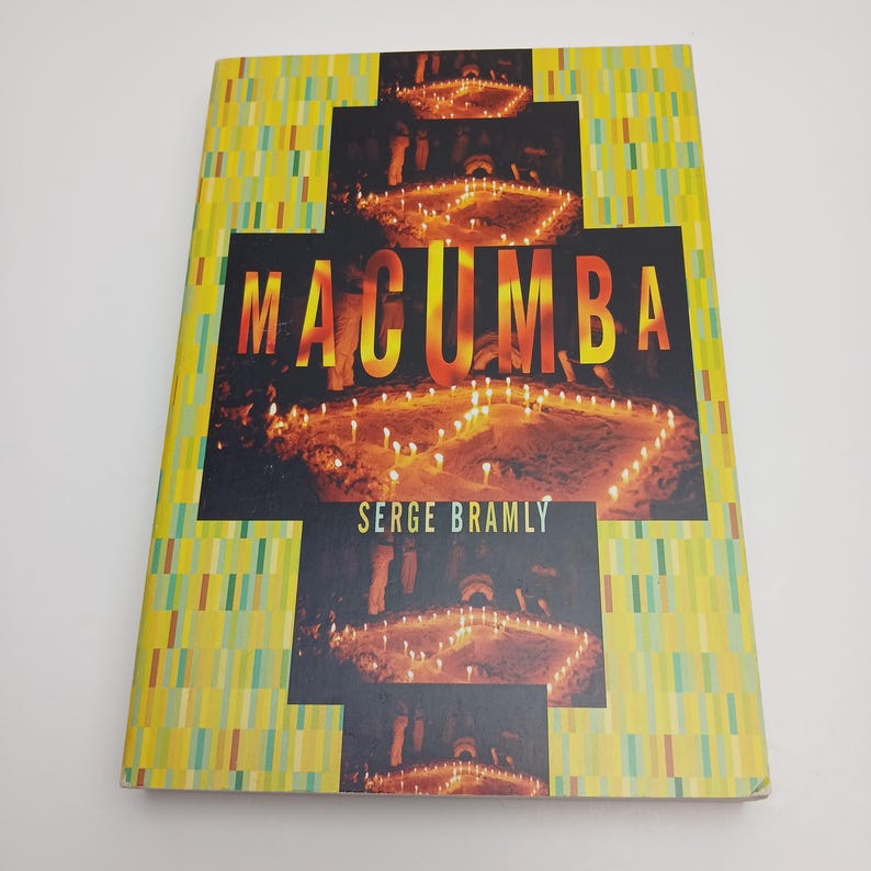Puede incluir: Un libro de tapa dura titulado Macumba de Serge Bramly. La portada presenta un borde con patr&oacute;n rectangular amarillo y verde que rodea un panel central negro con fotograf&iacute;as de velas encendidas dispuestas en formaci&oacute;n ritual.