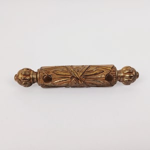 May include: A decorative bronze cabinet pull with intricate floral and geometric carvings. The pull features a rectangular central section with two circular mounting holes and rounded finials. The hardware is designed for furniture, such as drawers or cabinets.