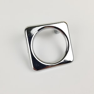May include: A square-shaped, chrome-plated cabinet knob with a round hole in the centre.