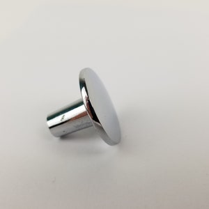 May include: A chrome-plated knob with a round, flat top and a cylindrical base. The knob is designed for use on furniture or cabinets.