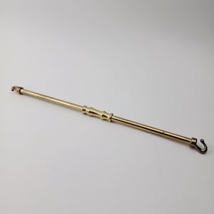 May include: A brass fireplace tool with a hook on one end and a decorative handle. The tool is long and slender, with a slightly curved hook. The brass has a warm, golden hue, and the tool appears to be vintage.