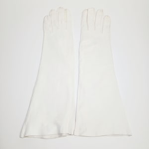 May include: A pair of long, solid white opera-length gloves. These gloves extend past the wrist and feature a smooth, opaque finish with stitched detailing along the fingers and a flared opening at the forearm, providing full hand and arm coverage.