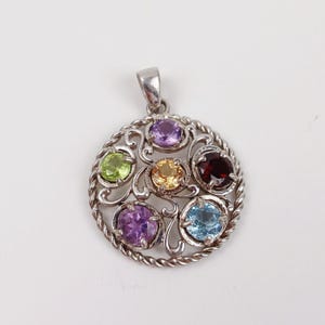 Puede incluir: Colgante de plata con un diseño circular, con siete piedras preciosas de colores. Las piedras preciosas incluyen piedras moradas, verdes, amarillas, rojas y azules. El colgante tiene un borde retorcido en forma de cuerda y adornos decorativos.