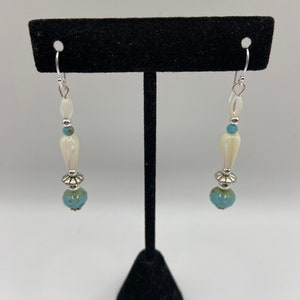 May include: A pair of dangle earrings with white and blue beads. The earrings are silver and have a teardrop shape.