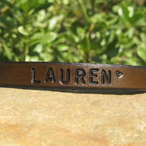 May include: A brown leather bracelet with the name "LAUREN" and a small heart engraved on it.
