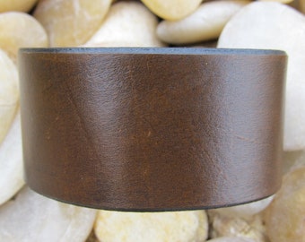 May include: A brown leather cuff bracelet with a dark brown edge.