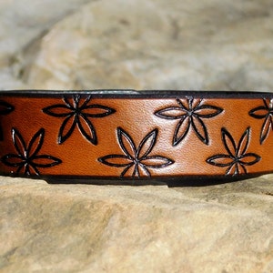 May include: A brown leather bracelet with a black floral pattern.