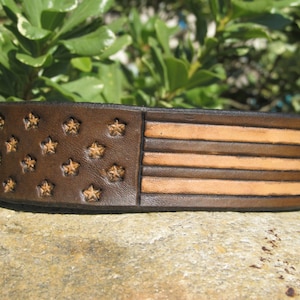 May include: A brown leather bracelet with an embossed American flag design. The stars are brown and the stripes are a lighter brown.