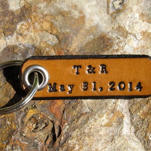 May include: A brown leather keychain with a silver key ring. The keychain has the text "T & R May 31, 2014" engraved on it.