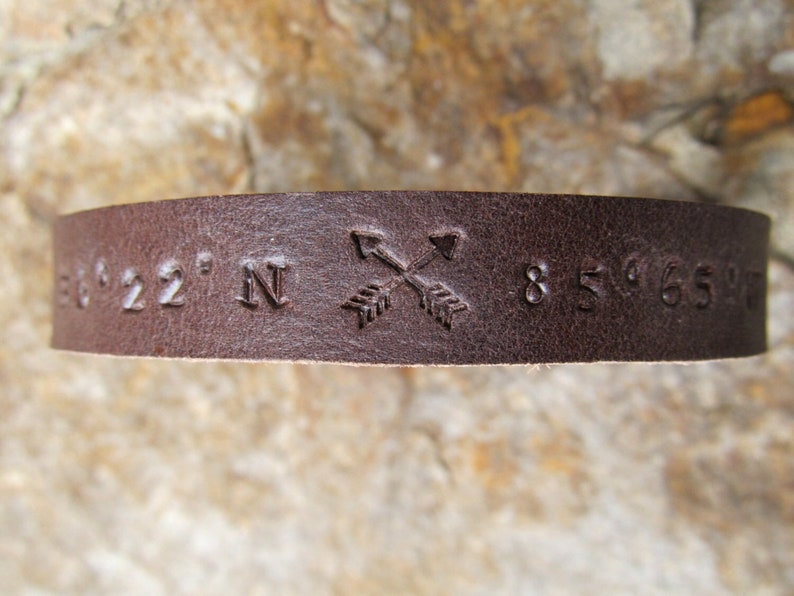 May include: Brown leather bracelet with coordinates 36&deg;22' N 85&deg;65' W and a pair of crossed arrows embossed on the front.