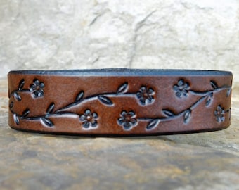 Peut inclure: Un bracelet en cuir marron avec un motif floral. Le bracelet est embossé avec un motif de vignes et de fleurs.