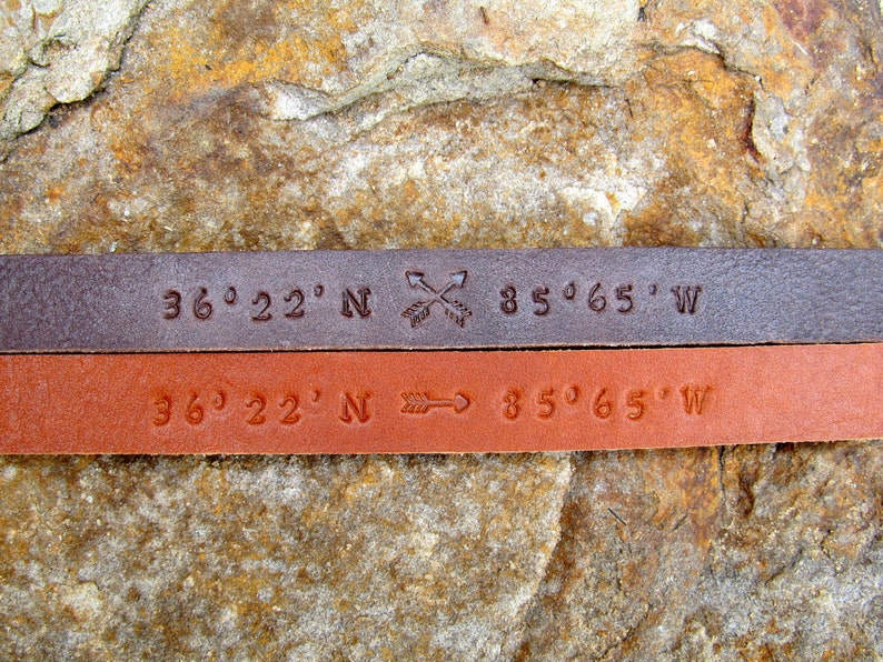 May include: Two leather bracelets with the coordinates 36&deg;22' N 85&deg;65' W engraved on them. One bracelet is brown and the other is a lighter brown.