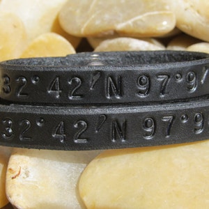 May include: Two black leather bracelets with the coordinates "32° 42' N 97° 97' W" embossed on them.