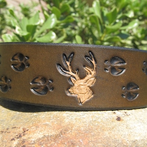 May include: A brown leather cuff bracelet with a deer head and paw prints embossed in black. The deer head is a light brown color.
