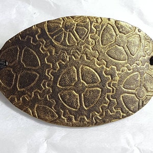 Puede incluir: Parche de ojo steampunk ovalado en bronce con diseño de engranajes. El parche para el ojo está hecho de un material metálico y tiene una banda elástica negra adjunta para usar. Los engranajes están grabados en la superficie, dándole una apariencia texturizada.