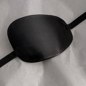 May include: A black eye patch with an elastic strap. The patch is made of a smooth, soft material.