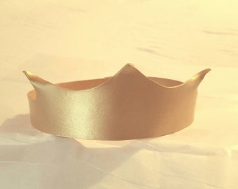 May include: A gold-colored cardboard crown with a simple design. The crown is made of a single piece of cardboard and has a smooth, shiny finish.