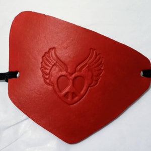 May include: Red leather eye patch with a peace sign heart and wings embossed on it.