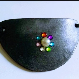 May include: A black leather eye patch with a decorative pearl and colorful rhinestones in the center.