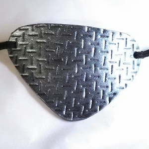 Op de afbeelding: Een metallic grijze ooglap met een ruitpatroon en een zwarte elastische band. De ooglap is ontworpen om één oog te bedekken en wordt waarschijnlijk gebruikt voor cosplay of kostuums.