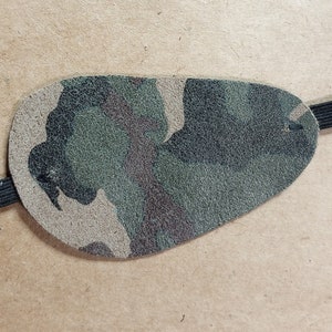 Puede incluir: Un parche para el ojo de camuflaje hecho de cuero con una correa elástica.