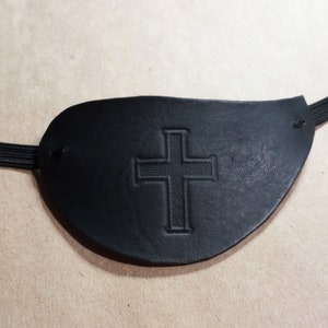 Puede incluir: Parche para el ojo de cuero negro con un diseño de cruz en relieve. El parche tiene una correa elástica.