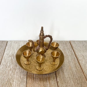 May include: A brass serving set with a teapot and six small cups on a decorative tray. The set is made of polished brass and has a traditional design.